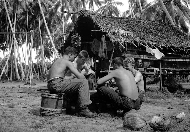 U.S. soldiers from every state shipped off to war. Here, after taking part in the fighting, soldiers (two from Detroit) relax by playing cards in a palm grove behind the lines at Buna, New Guinea on January 13, 1943. The players are, left to right: Pfc. Sam Demopolis, Detroit, Michigan,; Pfc. Robert Trudell (facing camera) of Detroit; Corp. James Williams (back to the camera); Genesee Depot, Wisconsin; and Pvt. Laurence Thompson, Duluth, Minnesota.