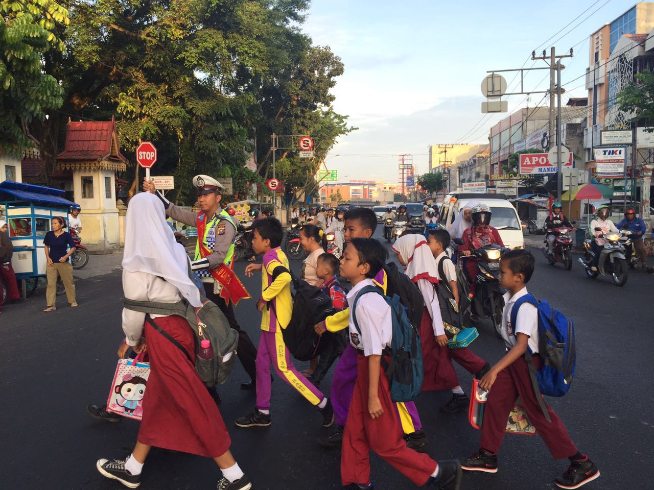 Personel Satlantas membantu menyeberangkan anak sekolah menggunakan rambu lalu lintas