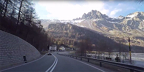 Day time drive in Switzerland. Image of a road winding by a river towards some mountains.