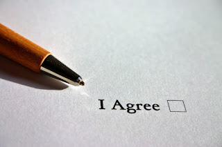 Stock photo of a ball-point pen lying on a piece of paper with a printed "I Agree" checkbox. The box is not checked.