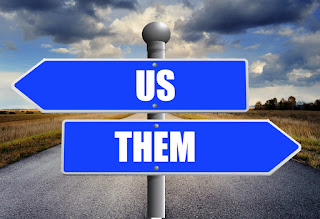 Directional road signs, one labelled 'us' pointing left, and one labelled 'them' pointing right.