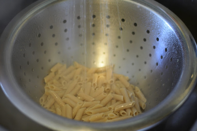 Fully cooked pasta in a strainer, being rinsed with water. 