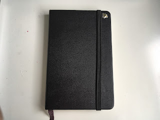 A black Moleskine notebook with a small bee sticker on the top right corner of the cover
