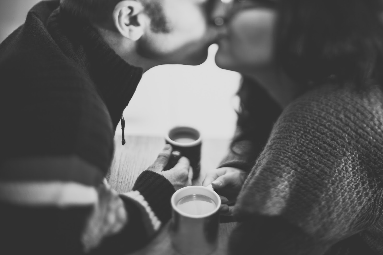Couple kissing, holding hands over a cup of coffee