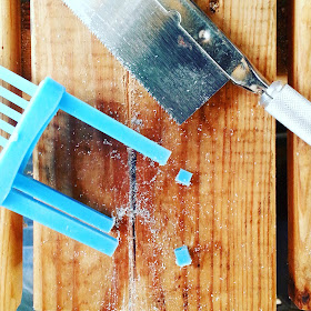 Plastic dolls' house miniature chair on a workbench next to a saw and pieces from the end of the chair legs.