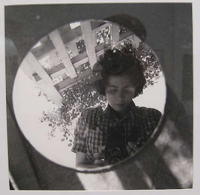 Young women with tousled dark hair photographing herself in a round mirror, set on the ground as if it were a hole in the ground