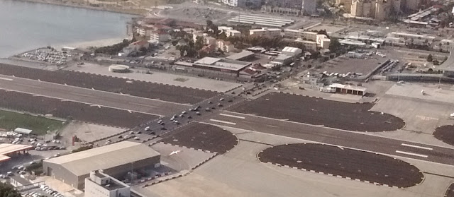 Photo of cars and other traffic crossing the runway of the Gibraltar airport after having waited for a plane to land. The road crossing the runway is the only land route in or out of the British territory which borders Spain.