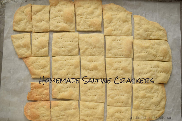 Golden, freshly-baked saltine crackers are presented on a baking sheet lined with parchement paper. 