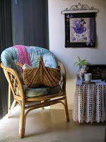 Bamboe leuningstoel en kleine tafel. Een korf met haaknaalden zit op de stoel.  Een kopje thee zit op de tafel.