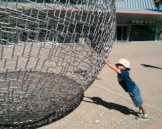 Little boy pushing up with his arms outstretched under the side of a large metal wire globe
