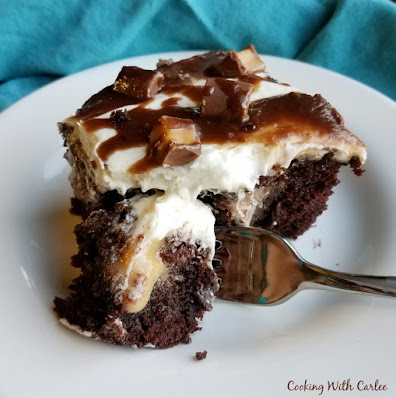 chocolate caramel poke cake with boiled milk frosting on top slice of rolo poke cake with fork taking first bite (chocolate cake, filled with caramel, topped wither ermine frosting and drizzled with fudge and chopped rolos)