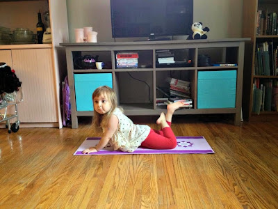 Photo of young girl sitting on a yoga mat on her tummy in the living room--with wooden floors