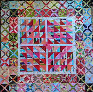 The top is made of multi-color striped triangles paired with reds. There are two rows of Crossroads blocks as an outer border.