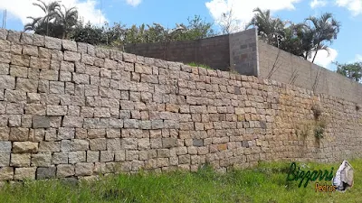 Construção do muro de pedra com pedra tipo pilastra de granito sendo um tipo de muro de pedra com junta seca com concreto e ferragem por trás por se tratar de uma muro de arrimo com pedras, podendo ser com esse tipo de assentamento de pedra ou com as pedras mais encaixadas ou com mais buracos entre as pedras.