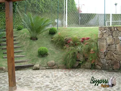 Detalhe do muro de pedra com o muro de pedra tipo faceado e o muro de pedra com pedras soltas sem cimento com nichos para colocação de plantas, o piso de pedra, a escada de dormente de madeira com execução do paisagismo em residência em Mairiporã-SP.