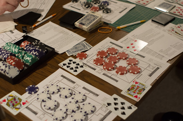 A table with assorted playing components, dice and playing cards, and play sheets and mats.