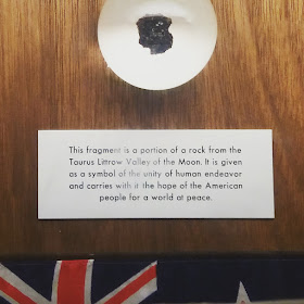 Piece of rock on a wall plaque. Underneath it is a sign saying'This fragment is a portion of a rock from the Tourus Littrow Valley of th eMoon. It is given as a symbol of the unity of human endeavor and carries with it the hope of the American people for a world of peace. Under the sign is a New Zealand flag.
