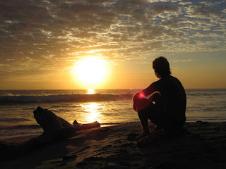 Silueta de un hombre sentado en la playa, mirando al atardecer.