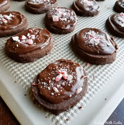 These peppermint mocha shortbread cookies are just like the coffee house drink but in chewable form. Put some on your Christmas cookie trays to take them to the next level! mocha shortbread cookies with chocolate frosting and bits of candy canes on cookie sheet