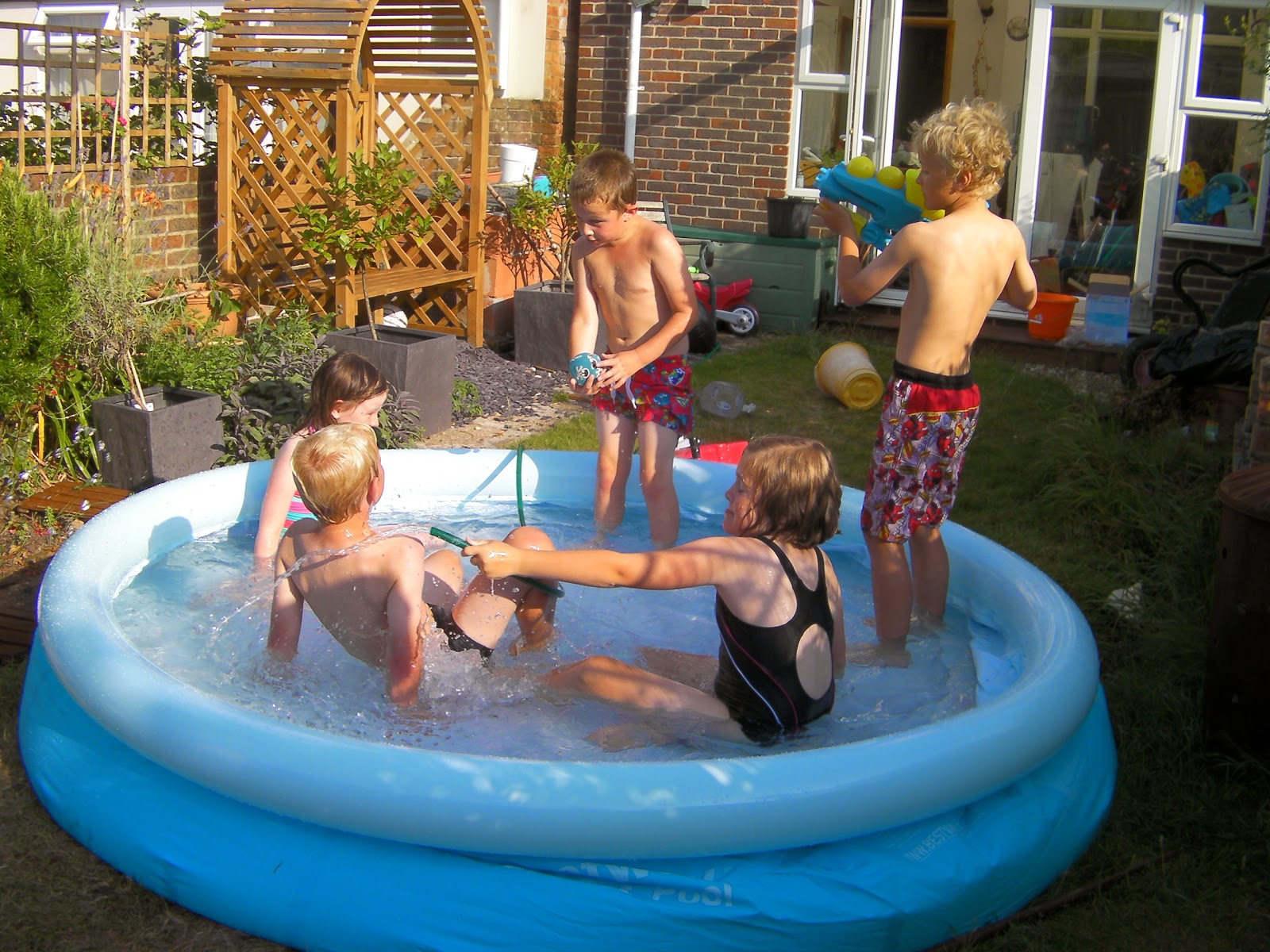 kids in paddling pool in back garden hosepipe games water pistol rifle in paddling pool