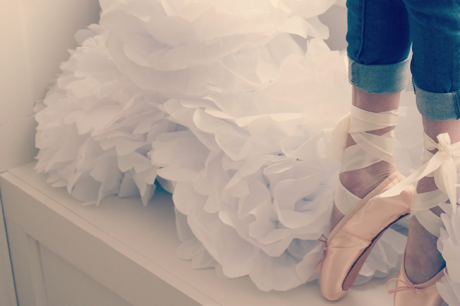 Michele of Hello Lovely Studio on pointe in pink ballet slippers at windowseat with white tissue poufs