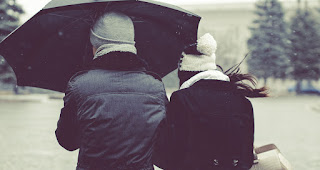 The couple are walking between winter park with black umbrella