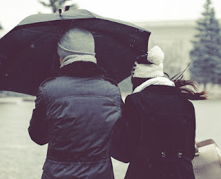 The couple are walking between winter park with black umbrella