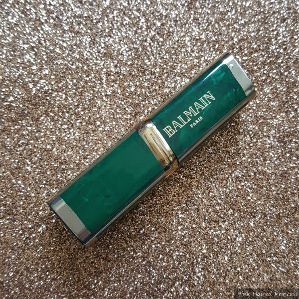 green marbled lipstick case with gold Balmain branding on glitter backdrop