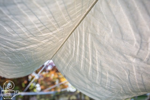 [Image of a natty woven wrap with an abstract stripe pattern hang drying in the summer shade outside with the fading light gently coming through the threads.]