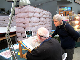 A woman watching a man stitching a very fine miniature carpet.