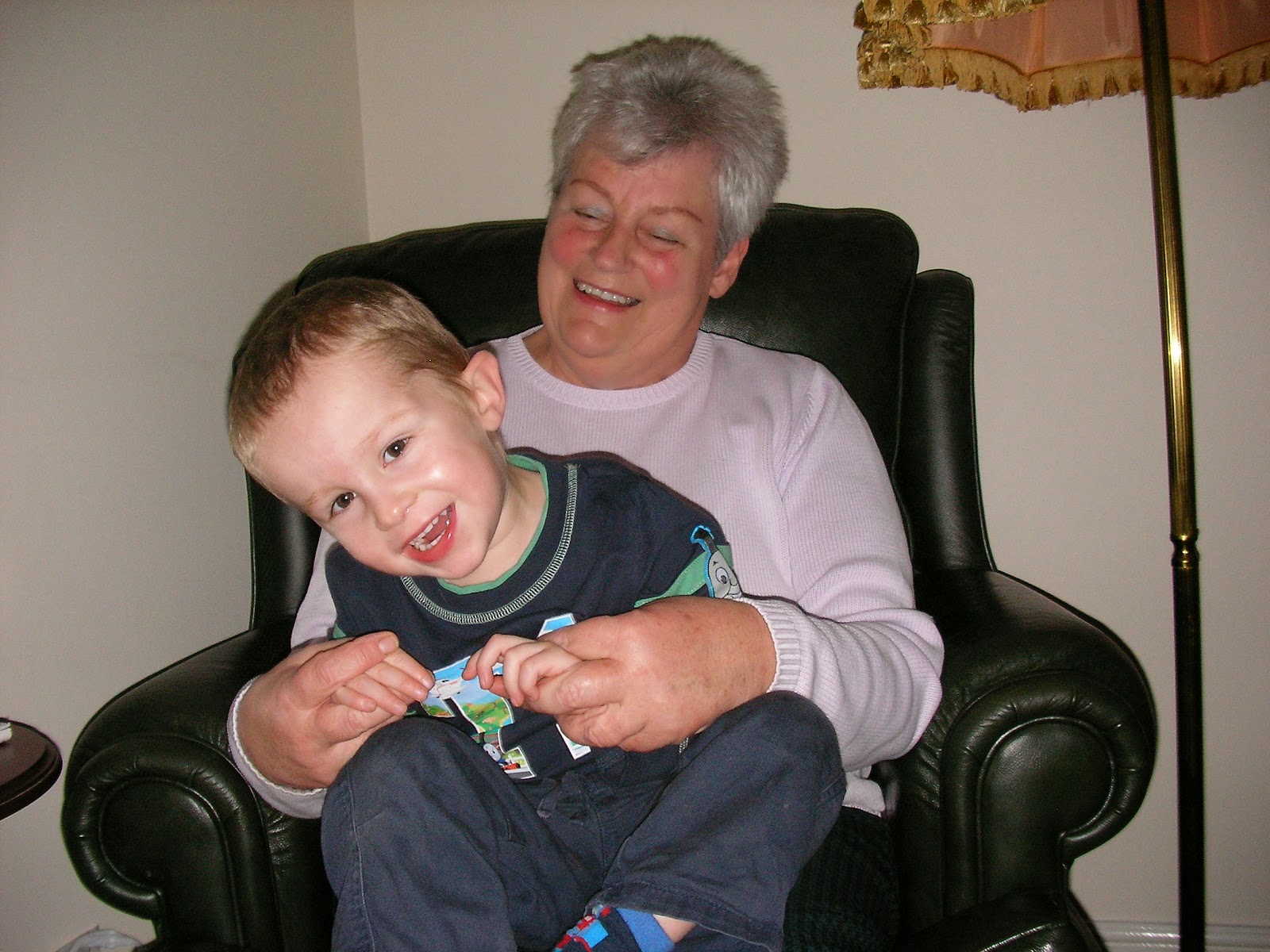 laughing grandmother tickling 2 year old grandson black leather armchair in new build house