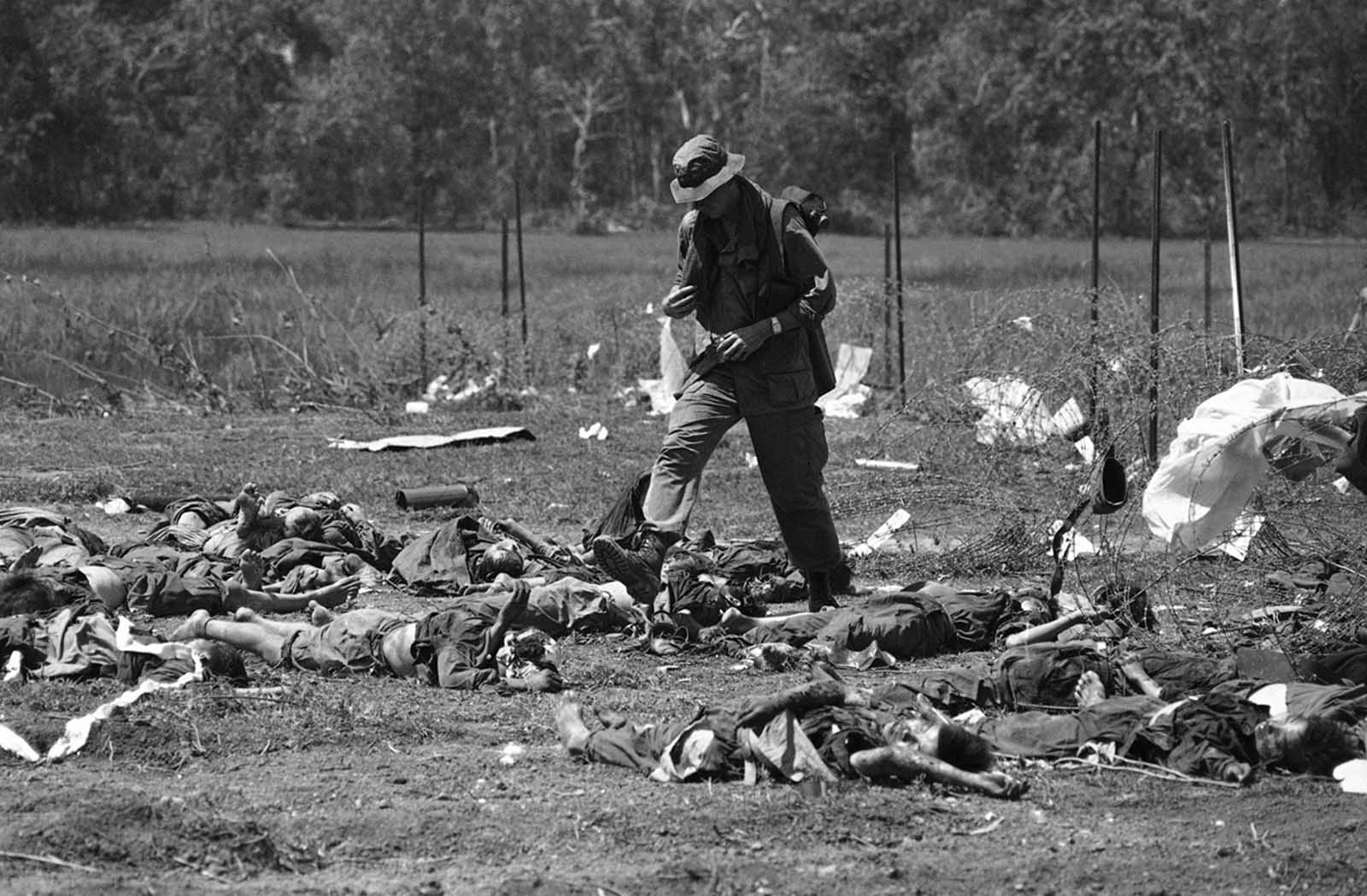 A GI of the U.S. 199th light infantry brigade walks through bodies laid out just outside the barbed wire perimeter of U.S. firebase crown in Cambodia on May 14, 1970. Fifty North Vietnamese were killed and only four Americans wounded when the North Vietnamese, presumably thinking the firebase already abandoned, walked into an ambush by the American defenders.