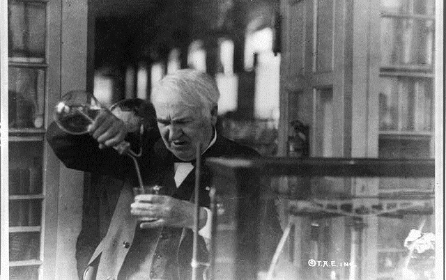 Image: Thomas Edison, half-length portrait, facing left and looking down into glass, experimenting in his laboratory, by Library of Congress/Public Domain on Picryl