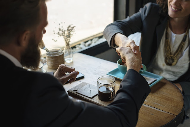 A man and woman shaking hands over coffee. 