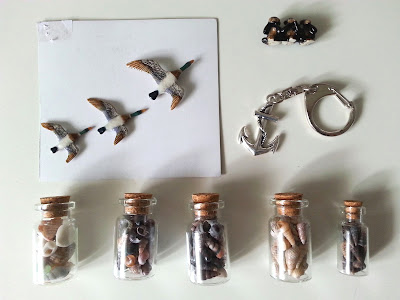 Miniature china flying ducks and wise monkeys, plus a metal anchor keyring and five bottles of miniature shells arranged on a tabletop.