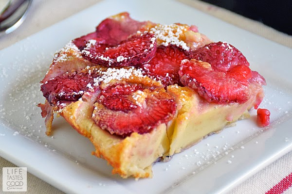 A beautiful slice of strawberry clafoutis sitting on a white plate and sprinkled with powdered sugar