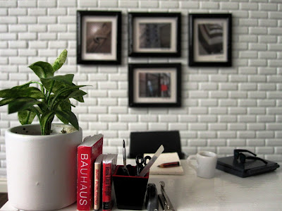 One-twelfth scale modern miniature architect's office with Eames chairs, a white table and architectural photos framed on the wall.