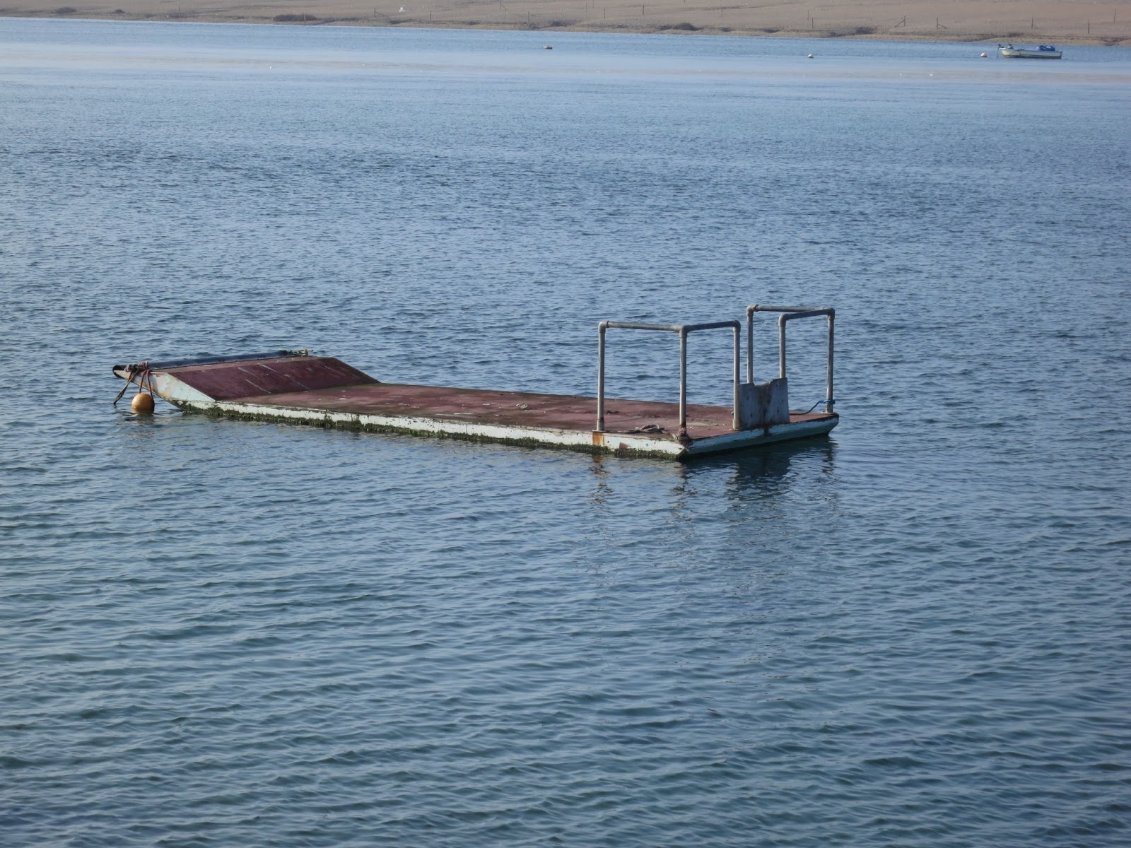 Platform with railing on Fleet Lagoon in Dorset. Blue water with ripples.