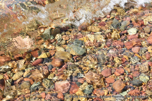 Colorful pebbles in the shallow water at the shore's edge.