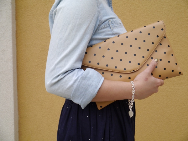 A detailed photo of a Madewell chambray shirt, J. Crew cognac leather belt and polka dot invitation clutch, Chinti and Parker skirt from Vancouver boutique Oliver and Lilly's, and a silver charm bracelet from Birks.