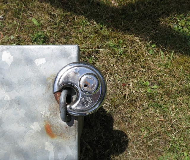 Shiny padlock on metal box with rust on grass with shadows of fence