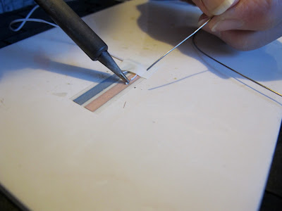 Woman soldering a length of wire onto copper tape.