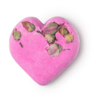A light pink coloured heart shaped bath bomb with seven yellow rose petals encrusted into the bath bomb on a white background.