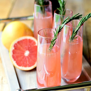 Rosemary Pink Grapefruit Mimosas - This twist on the traditional orange juice mimosa results in a bright, but tart, herbal drink. Perfect for a special brunch and the pretty pink color with the green of the rosemary is a show stopper. #cocktail #alcohol #champagne #mothersday #brunch | bobbiskozykitchen.com Rosemary Pink Grapefruit Mimosas on a wooden serving tray