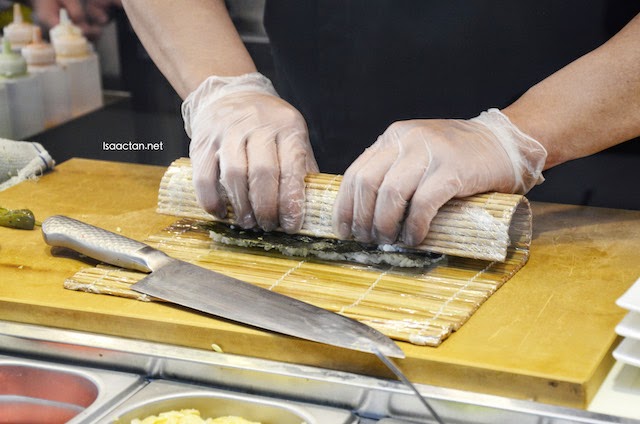 Okonomi prepares the sushi rolls in front of you behind a transparent glass