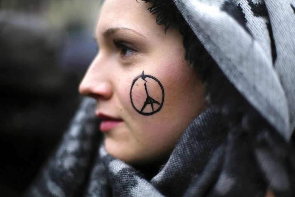 70 Of The Most Touching Photos Taken In 2015 - A woman has a peace sign combined with the Eiffel Tower painted on her face for a minute of silence outside the French Embassy in Berlin in memory of the 130 killed in the November Paris attacks.
