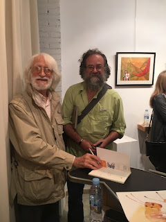 Photo of two smiling men looking at us. From left to right:  Enric Lareulla ( catalan writer ) and George Pratt ( American Artist)  The writer signed a book for the Artist.