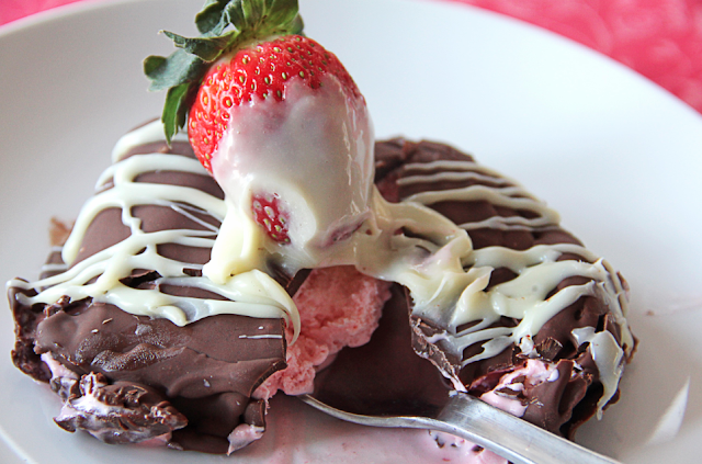 Close up of a chocolate covered strawberry klondike bar cut into with a spoon.