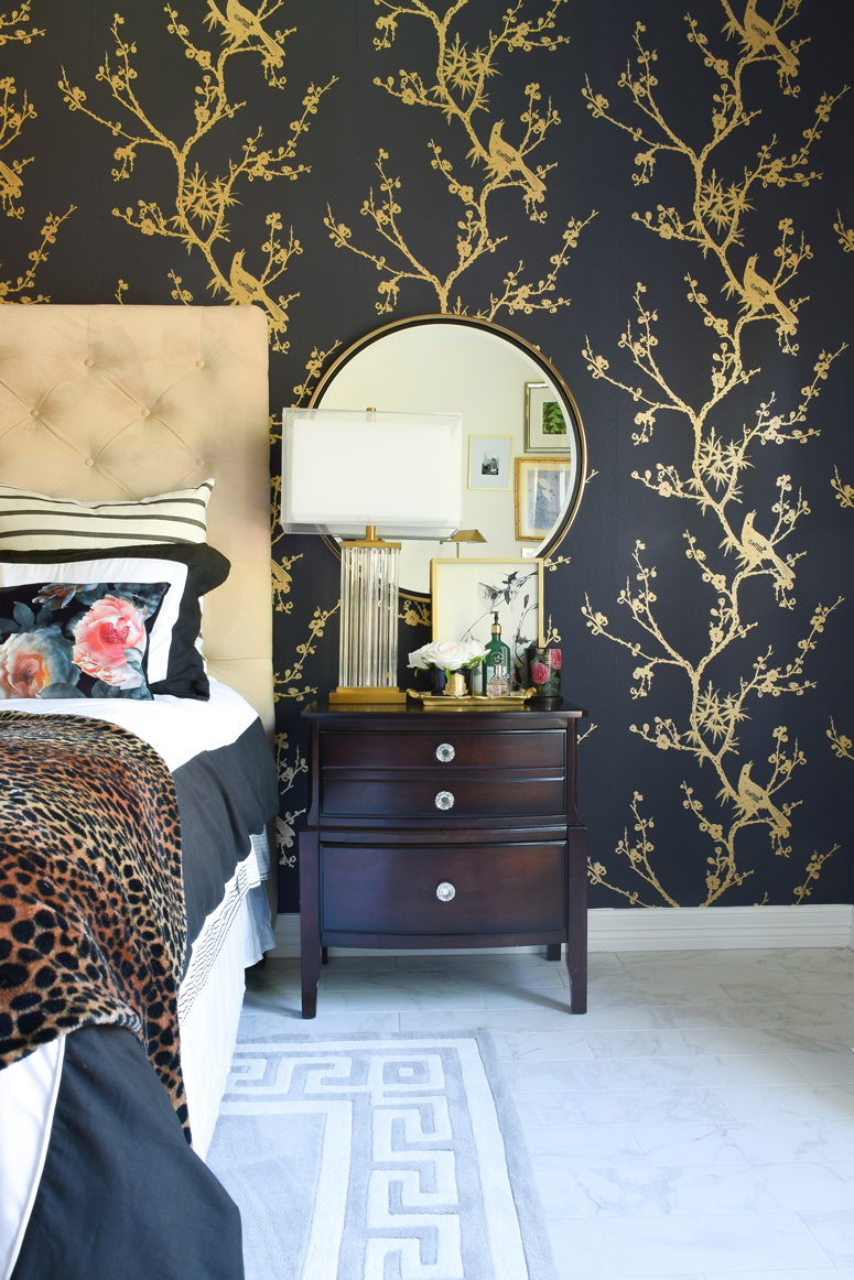 Dark nightstands add drama to a black and gold wallpaper accent wall. The mirror and crystal lamp brighten the space.