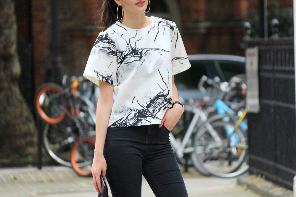 peexo fashion blogger wearing ink print top and ripped black jeans and clutch